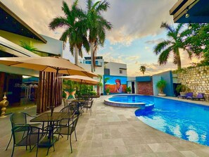 An outdoor pool area with lounge chairs, umbrellas, and a mural on the wall. - Grann Hotel (Ciudad Valles)