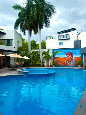 A swimming pool with a mural, palm trees, and modern buildings. - Grann Hotel (Ciudad Valles)