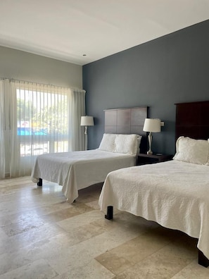 Habitación de hotel con dos camas, un ventanal con cortinas y vista a una piscina.