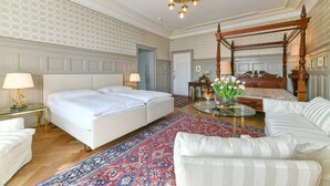 A hotel room with a four-poster bed, a sitting area with a glass coffee table, and a large patterned rug.