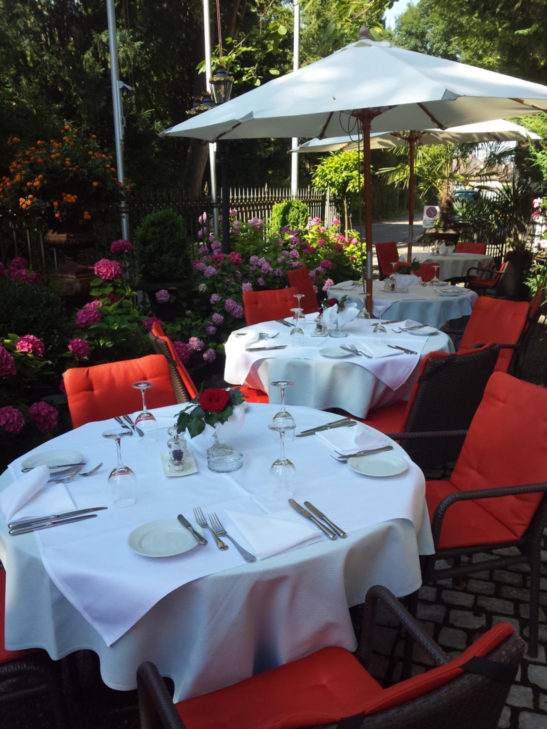 Outdoor dining tables set with white tablecloths, red chairs, and umbrellas.