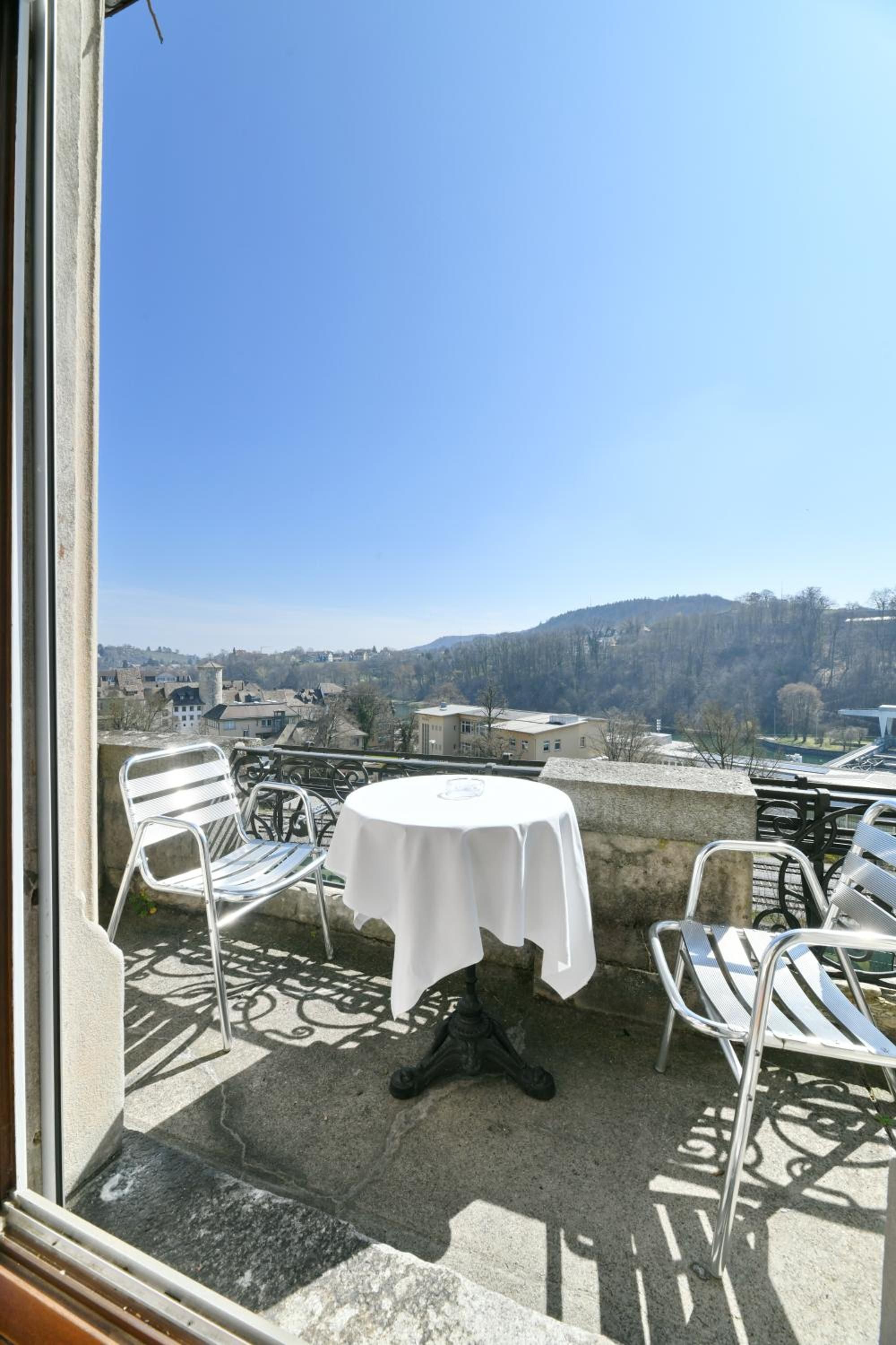 A balcony with a table and chairs, overlooking a town and hills.