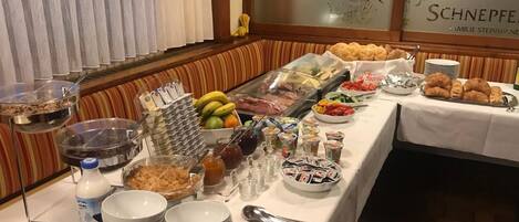 A buffet table with various food items and utensils, including fruits, pastries, and condiments.