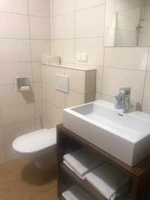 A bathroom with a white sink, a toilet, and a towel shelf. - Schnepfenhof (Jois)