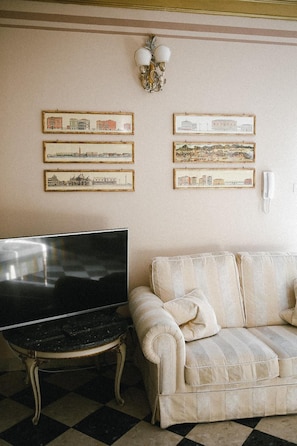 A room with a television on a stand, a sofa, and framed cityscape pictures on the wall. - Martins Residence De Luxe (Ravenna)