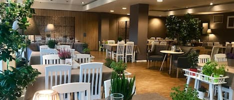 Un comedor de hotel con varias mesas y sillas, algunas decoradas con plantas.