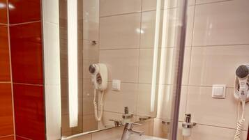 A modern bathroom with a glass shower enclosure, a sink with a mirror, and two hair dryers mounted on the wall.
