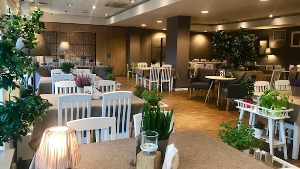 Área de jantar de hotel com várias mesas e cadeiras, algumas com plantas.