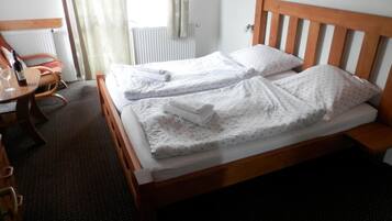 Habitación de hotel con cama de madera, dos almohadas, una mesita con una botella y una silla.
