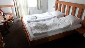 Ein Hotelzimmer mit einem hölzernen Bett, zwei Kissen, einem kleinen Tisch mit einer Flasche und einem Sessel.