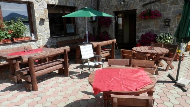 Eine Terrasse im Freien mit Holztischen und -bänken, Steinmauern und Blumentöpfen.