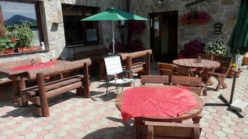 Un patio exterior con mesas y bancos de madera, paredes de piedra y plantas en macetas.
