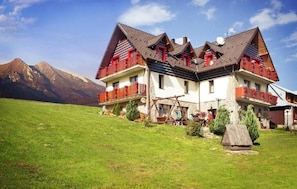 Een chalet met twee verdiepingen, een schuin dak, houten balkons en een stenen fundering.