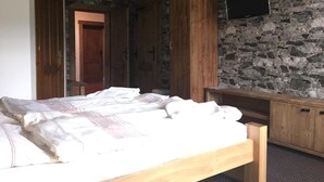 Ein Schlafzimmer mit einem hölzernen Bett, einer Steinwand und einem wandmontierten Flachbildfernseher.