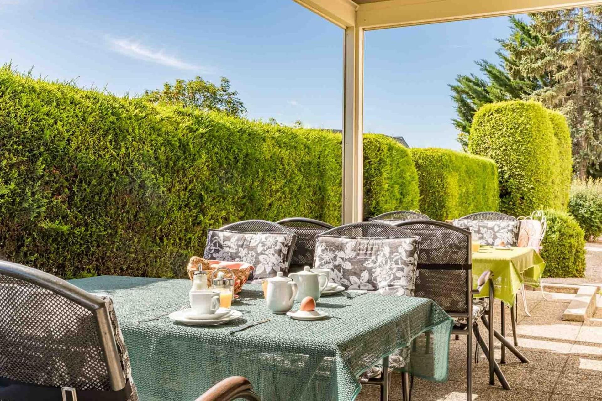 An outdoor patio with a table set for tea, surrounded by chairs with patterned cushions, under a clear sky.