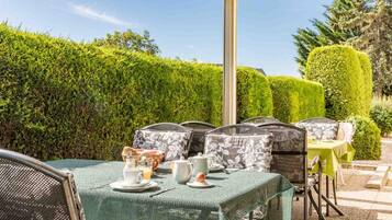 An outdoor patio with a table set for tea, surrounded by chairs with patterned cushions, under a clear sky.