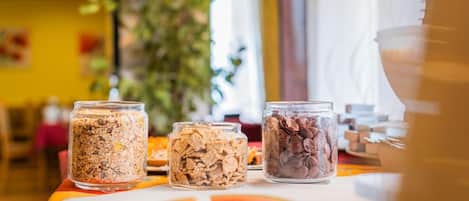 Three glass jars containing different types of cereal on a table with a slice of watermelon.