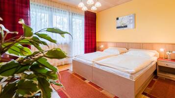 A double bed with a wooden headboard, a bedside table with a lamp, and a window with sheer curtains.