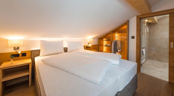 A hotel room with a large bed, bedside tables, a built-in wardrobe, and a shower area. - Tiroler Weinstube (Seefeld in Tirol)