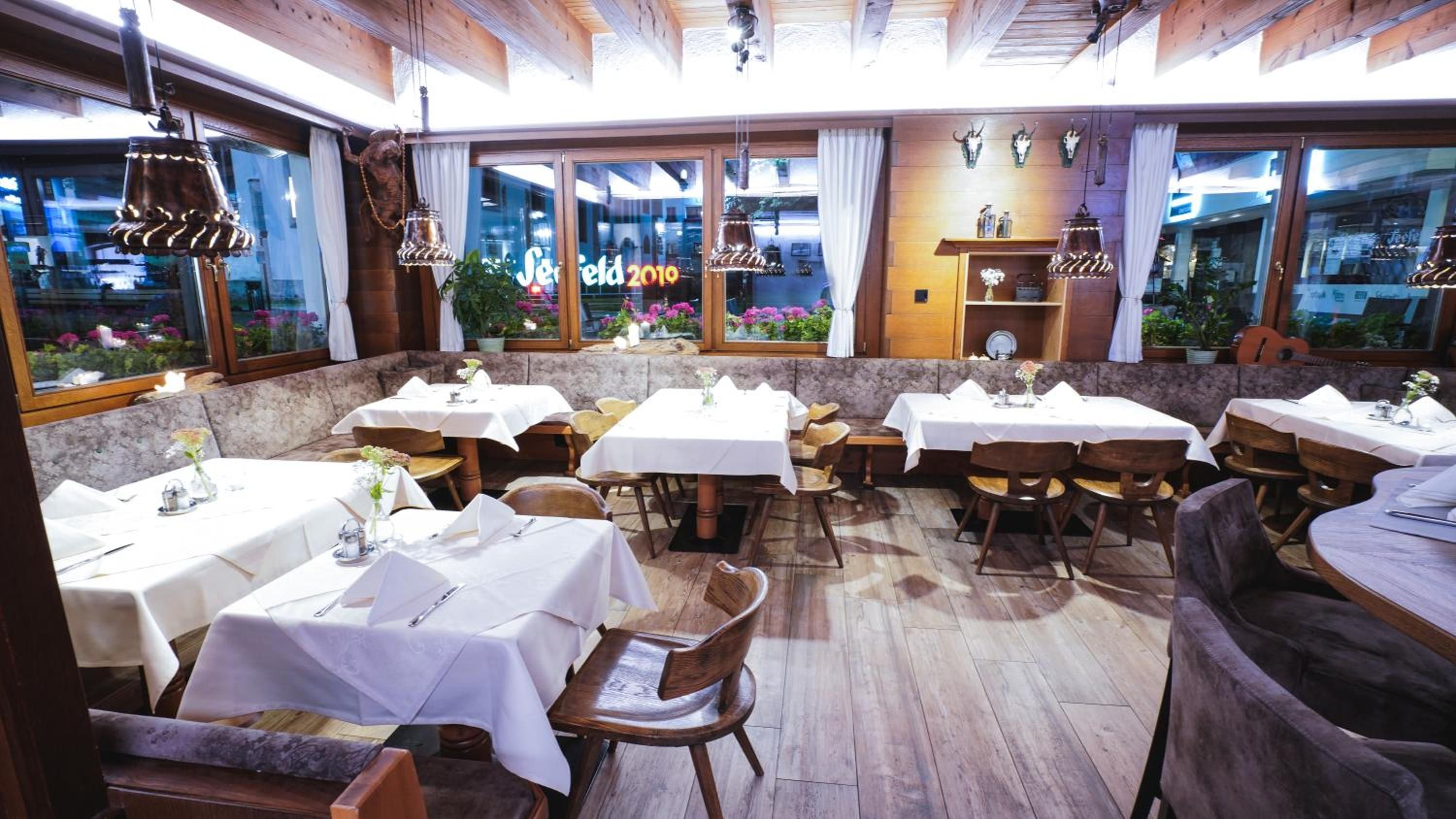 L’intérieur d’un restaurant, avec de nombreuses tables et chaises, un plancher en bois et de grandes fenêtres ornées de rideaux.