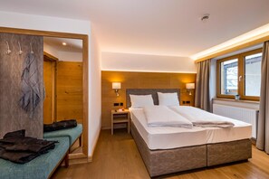 A hotel room with a large bed, bedside lamps, a wooden headboard, a bench with a bag, and a window with curtains. - Tiroler Weinstube (Seefeld in Tirol)