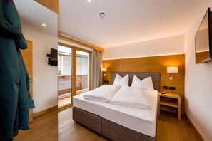 A hotel room with a bed, a nightstand, a lamp, a mirror, and a view of the outside. - Tiroler Weinstube (Seefeld in Tirol)