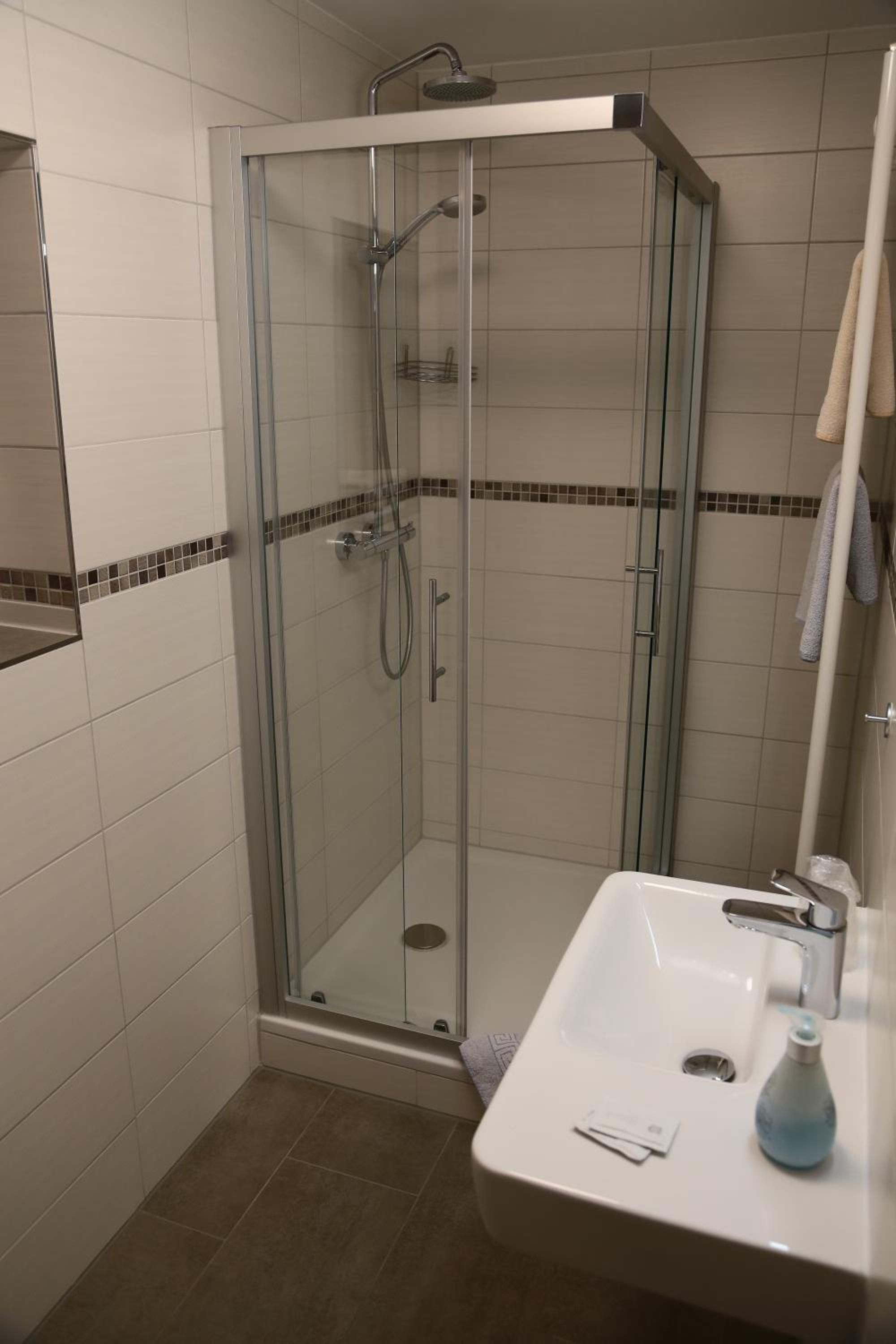Eine begehbare Glasdusche mit Duschbrause, ein Waschbecken mit Armatur und ein Spiegel darüber.