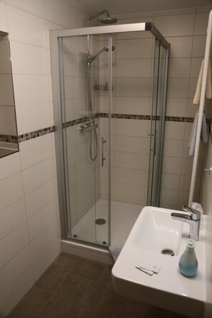 Una ducha con mampara de vidrio, un cabezal de ducha manual, un lavamanos con grifo y un espejo sobre el lavamanos.