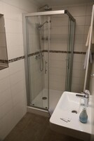 Una ducha con mampara de vidrio, un cabezal de ducha manual, un lavamanos con grifo y un espejo sobre el lavamanos.