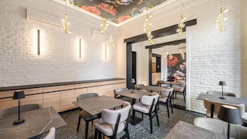 A restaurant interior with brick walls, marble flooring, and pendant lighting. Tables and chairs are arranged for dining.