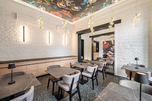 A restaurant interior with brick walls, marble flooring, and pendant lighting. Tables and chairs are arranged for dining.