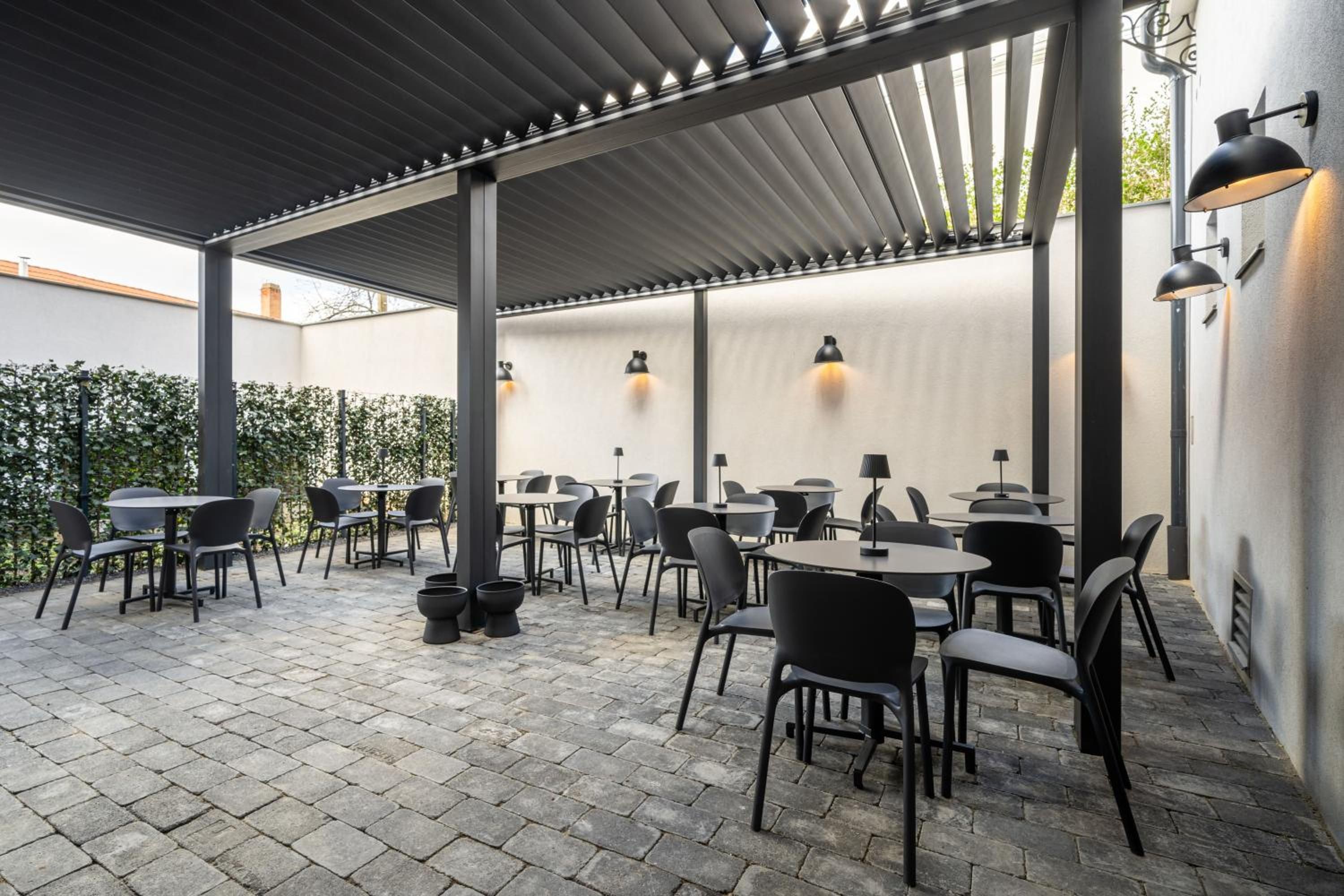 Un patio al aire libre con mesas y sillas, una pérgola y luces fijadas a la pared.
