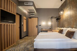 A hotel room with a large bed, a wooden wardrobe, a flat-screen TV, a desk with a chair, and a mirror.