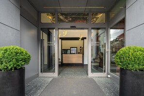 A hotel entrance with a reception desk, glass doors, and two potted plants.