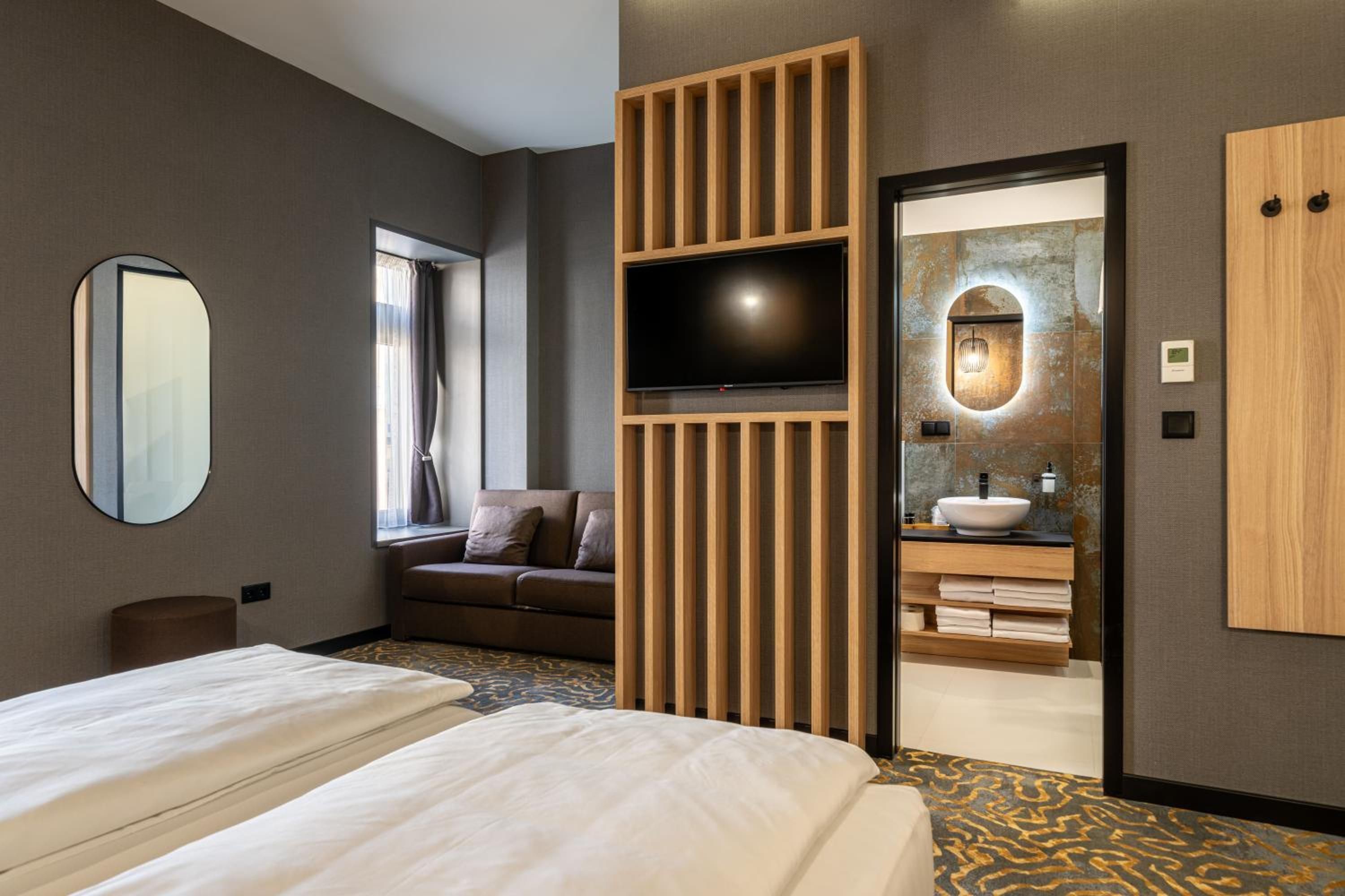 Una habitación de hotel con una cama, un sofá, un televisor, un baño con lavamanos y un espejo.