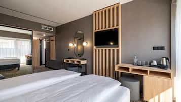 A hotel room with a large bed, a desk with a mirror, a television, and a kitchenette area.
