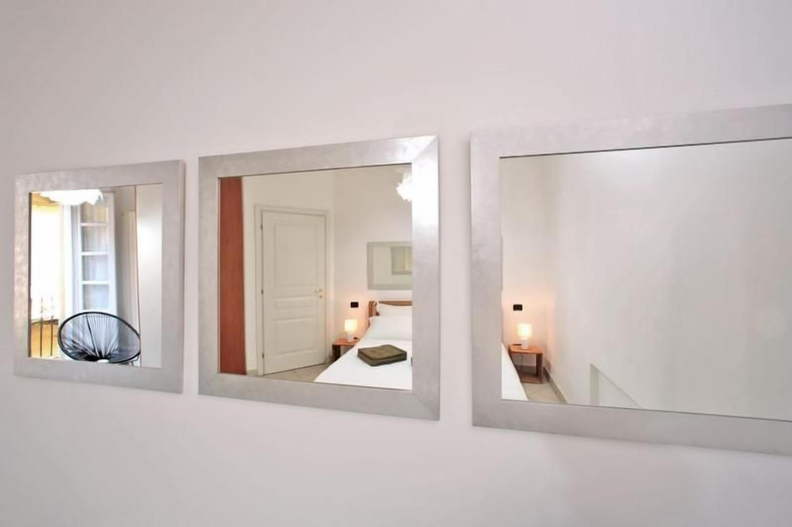 Three wall-mounted mirrors with reflections of a room, a chair, and a bed.