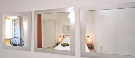 Three wall-mounted mirrors with reflections of a room, a chair, and a bed.
