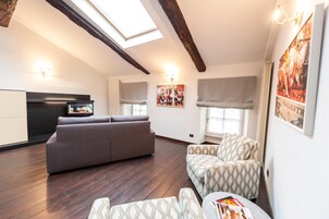 A modern living space with a sofa, patterned armchairs, a television, and artwork on the walls.