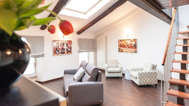 A spacious loft with a high ceiling, wooden beams, a skylight, and a staircase.