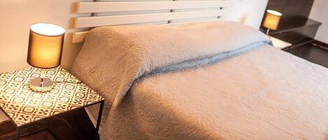 A hotel room with a bed, a bedside table, a lamp, and a wall-mounted switch.