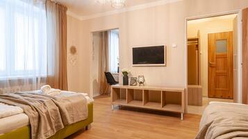 A hotel room with two beds, a TV, a bedside table with decorative items, and a door leading to another room.