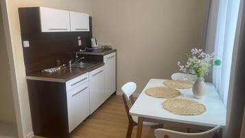 Una cocina compacta con armarios blancos, cafetera y una mesa de comedor con individuales y un florero.
