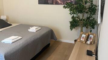 Habitación de hotel con una cama, un escritorio, una planta en maceta, un televisor de pantalla plana y un cuadro con una vista urbana en la pared.