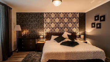 Un dormitorio con una cama grande, cabecera de madera oscura, papel tapiz estampado, lámparas de noche y cuadros en la pared.