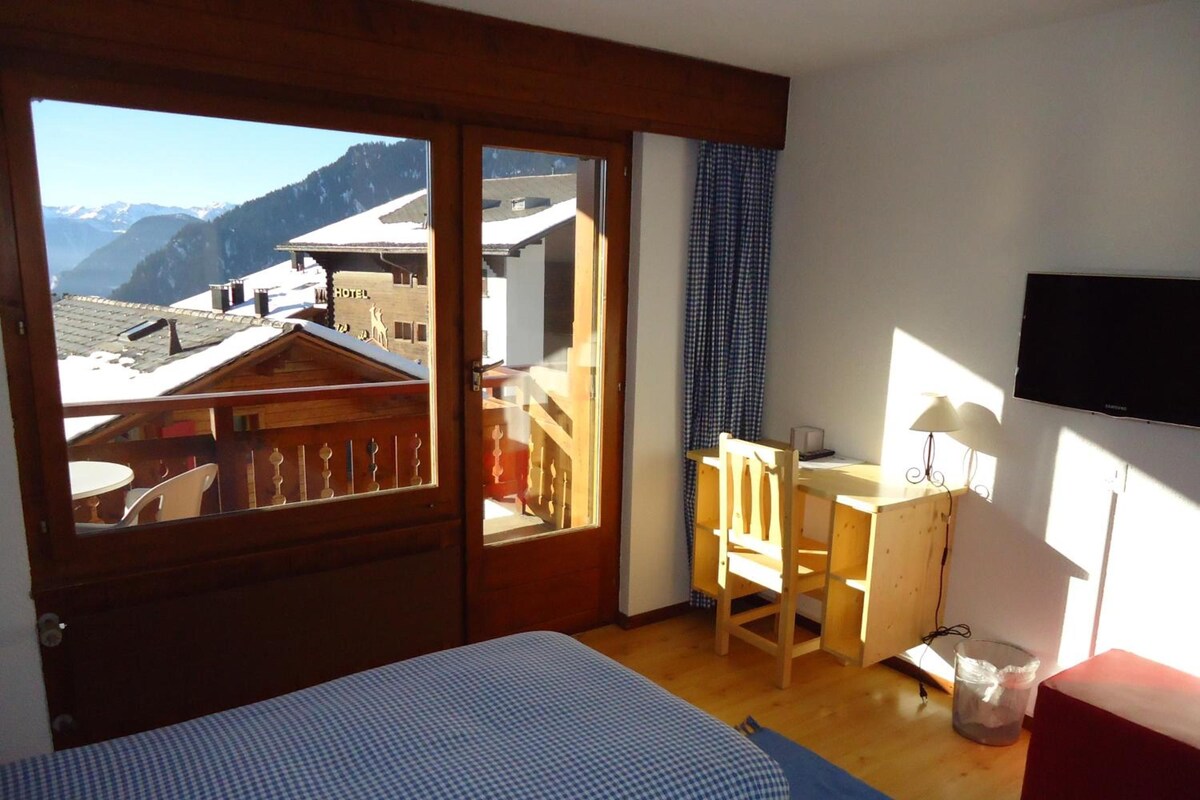 Una habitación con cama, escritorio, silla, televisor y vistas a la montaña.