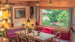 A cozy cabin interior with a wooden dining table, cushioned seating, and a window offering a view of greenery. - Hotel Mirabeau (Bagnes)
