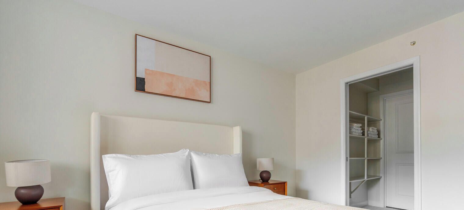 Une chambre d’hôtel comprenant un lit, deux tables de chevet, une commode, une armoire et un tableau encadré au mur.