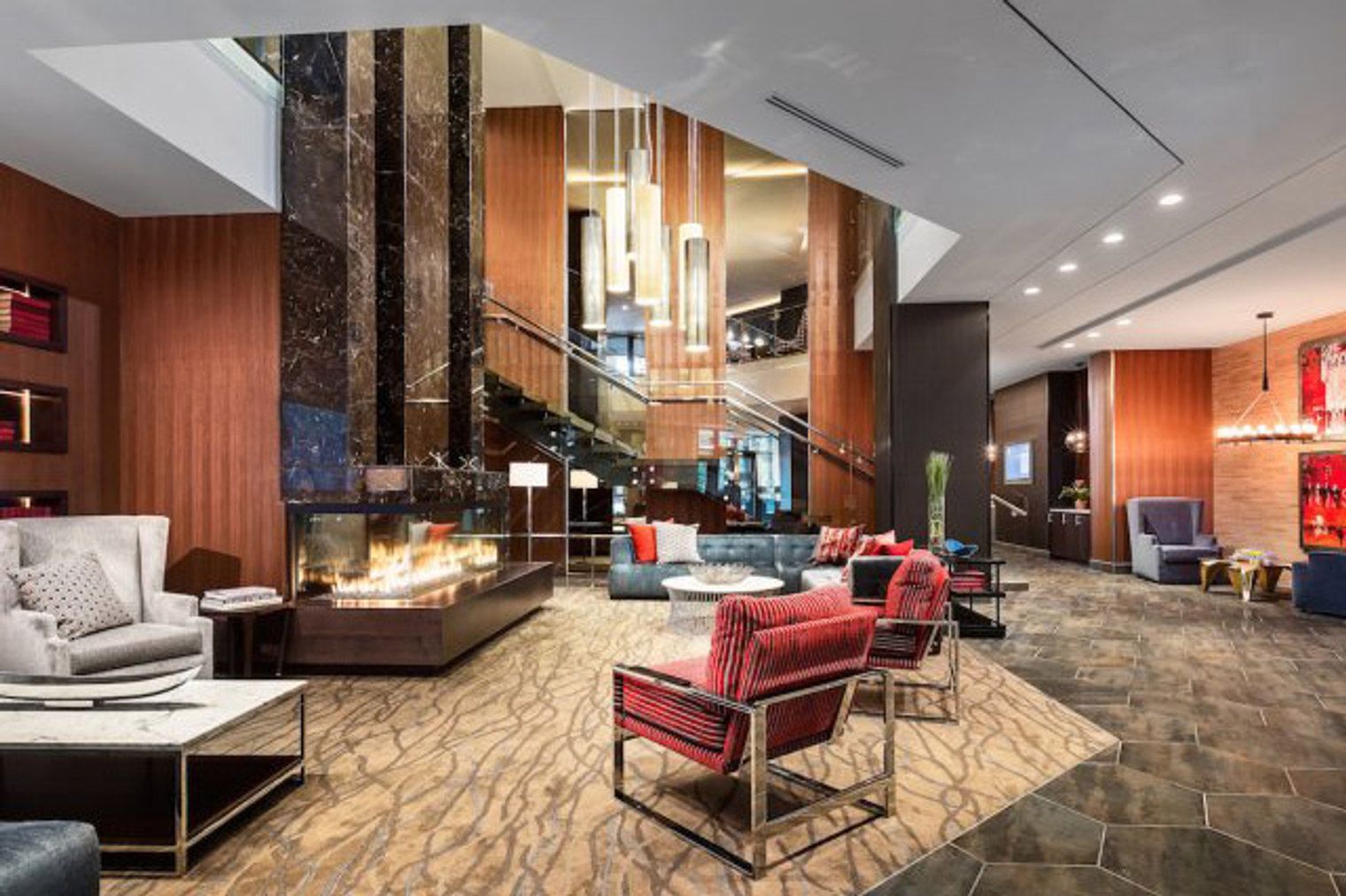 A modern lobby with a fireplace, comfortable seating, a staircase, and a large chandelier.