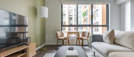 A modern living room with a flat-screen TV, a coffee table, a sofa, and two chairs.